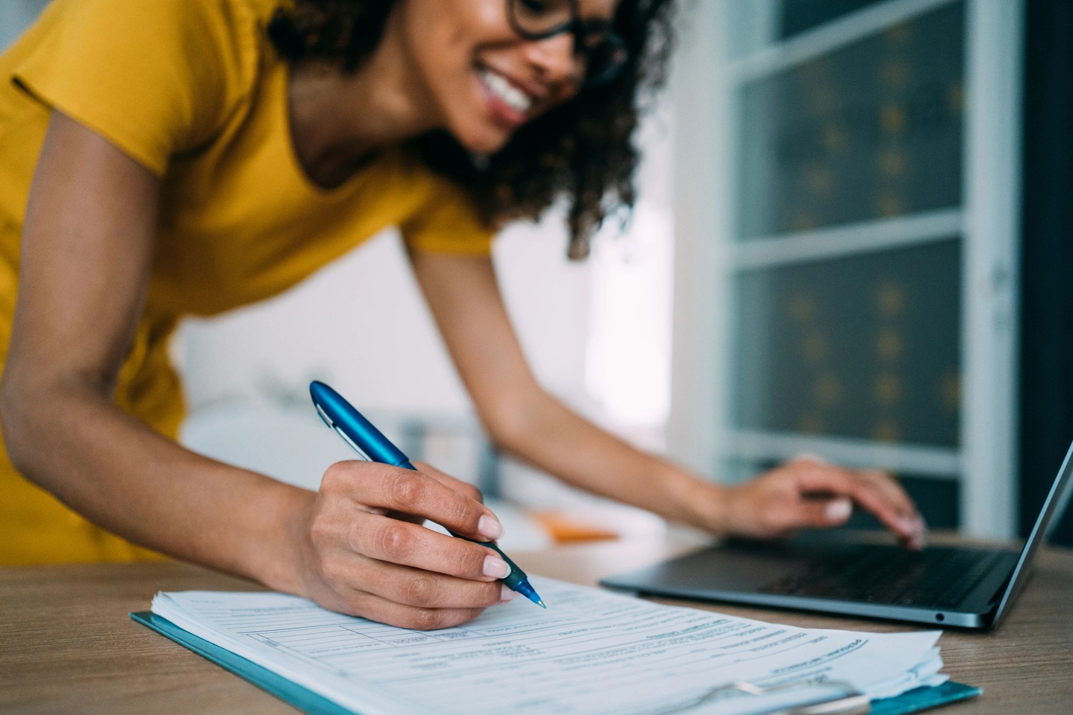 Person completing paperwork while working on a laptop